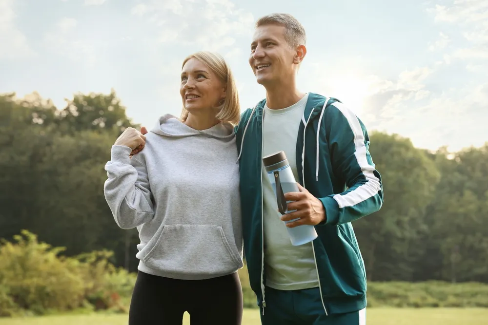 A happy middle aged man and woman walk outdoors in atheletic wear.